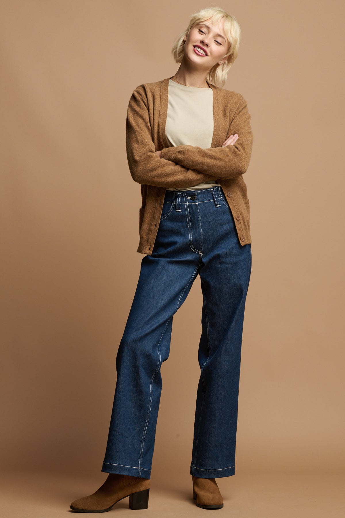 
            female wearing lambswool cardigan open over stone t shirt paired with work trousers in blue and camel coloured boots