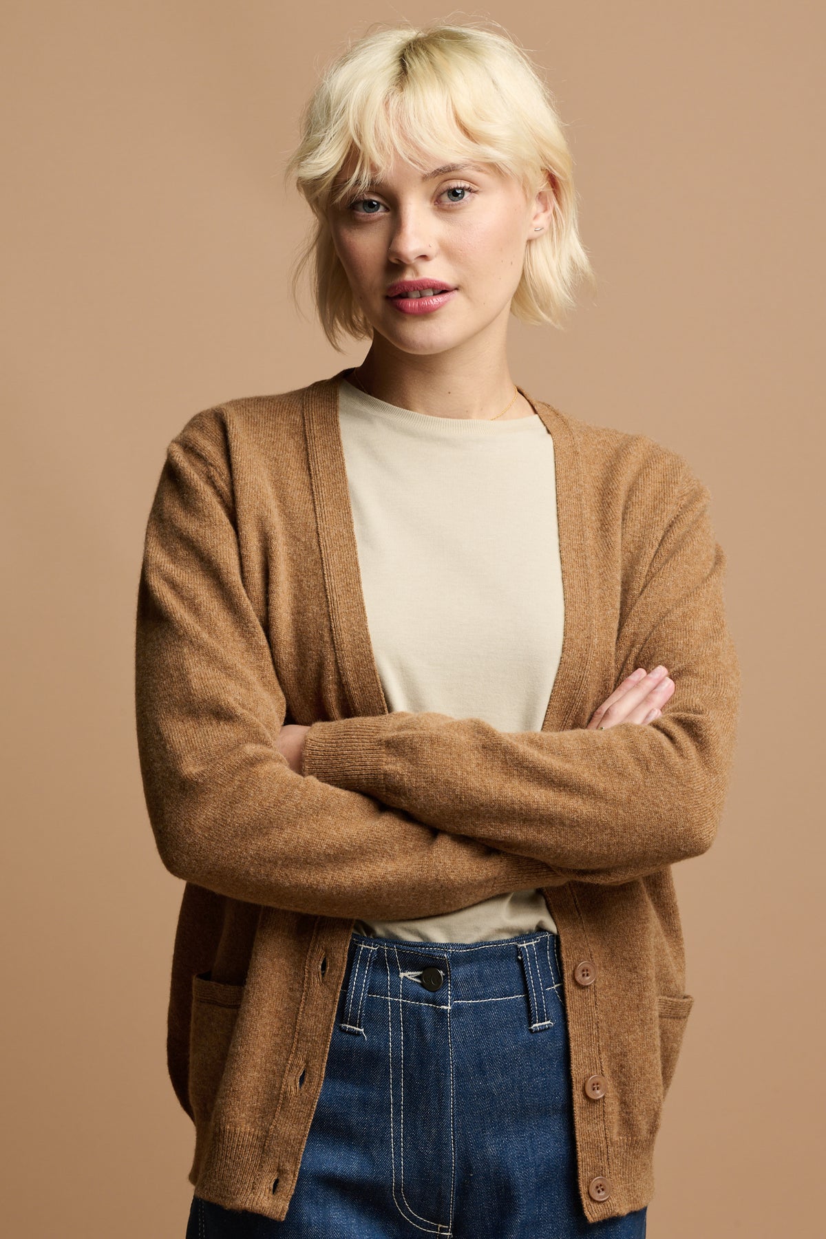 
            Thigh up image of female with blonde hair wearing unbuttoned lambswool cardigan in dark camel