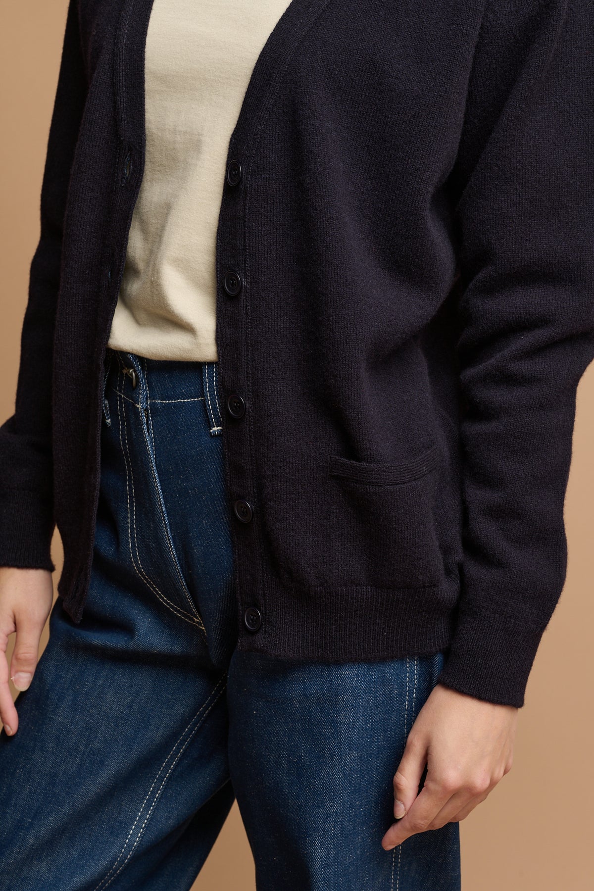 
            Close up of lambswool cardigan in navy unbuttoned over work jeans in blue