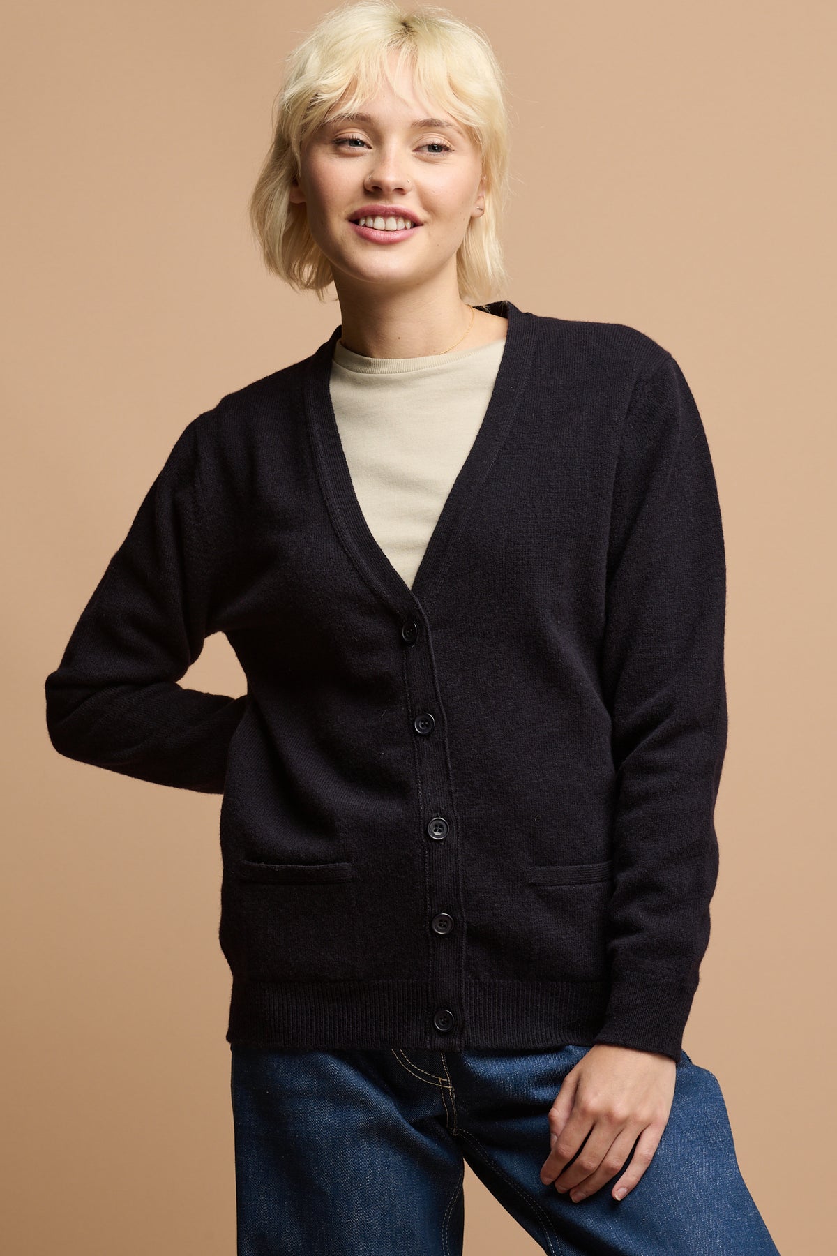 
            Thigh up of female wearing buttoned up lambswool v neck cardigan in navy over crew neck t shirt in stone 