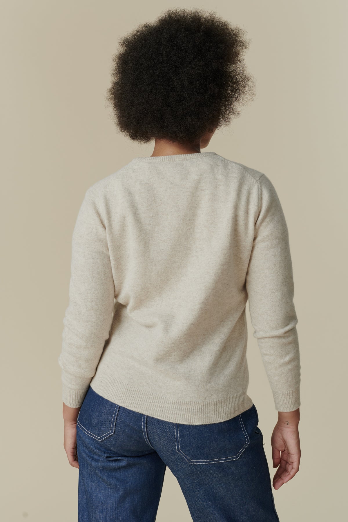 Thigh up image of back of female wearing lambswool crew neck jumper in linen