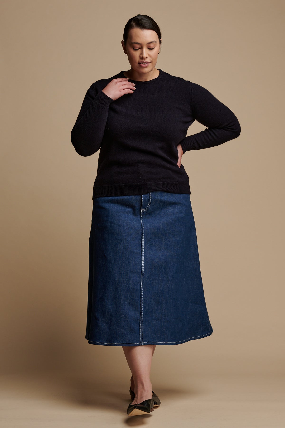 Full body of the front of female wearing lambswool crew neck jumper in navy paired with Bobbie a line denim midi skirt in blue.