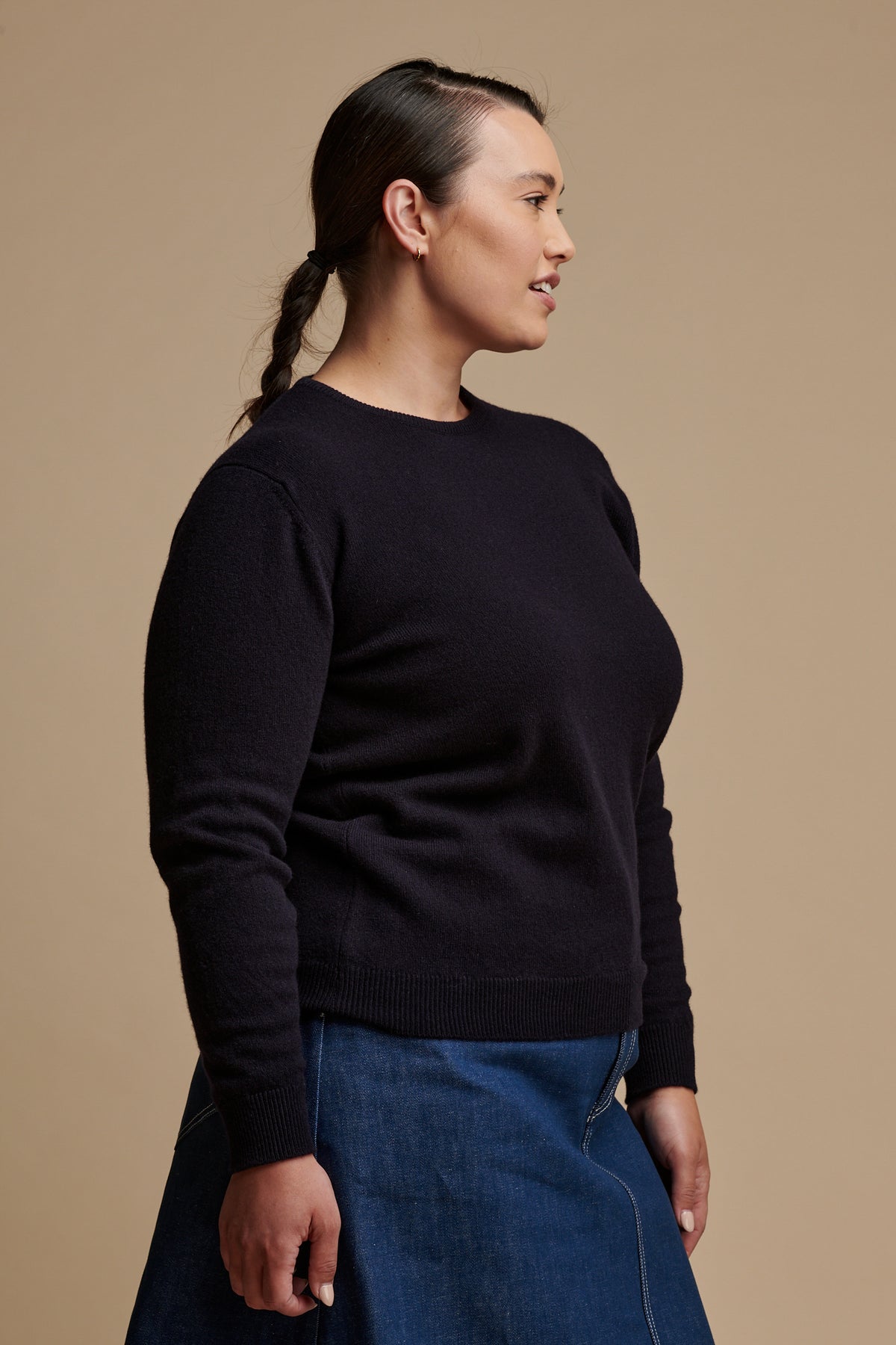 Thigh up of the side of female wearing lambswool crew neck jumper in navy paired with Bobbie a line denim midi skirt in blue.