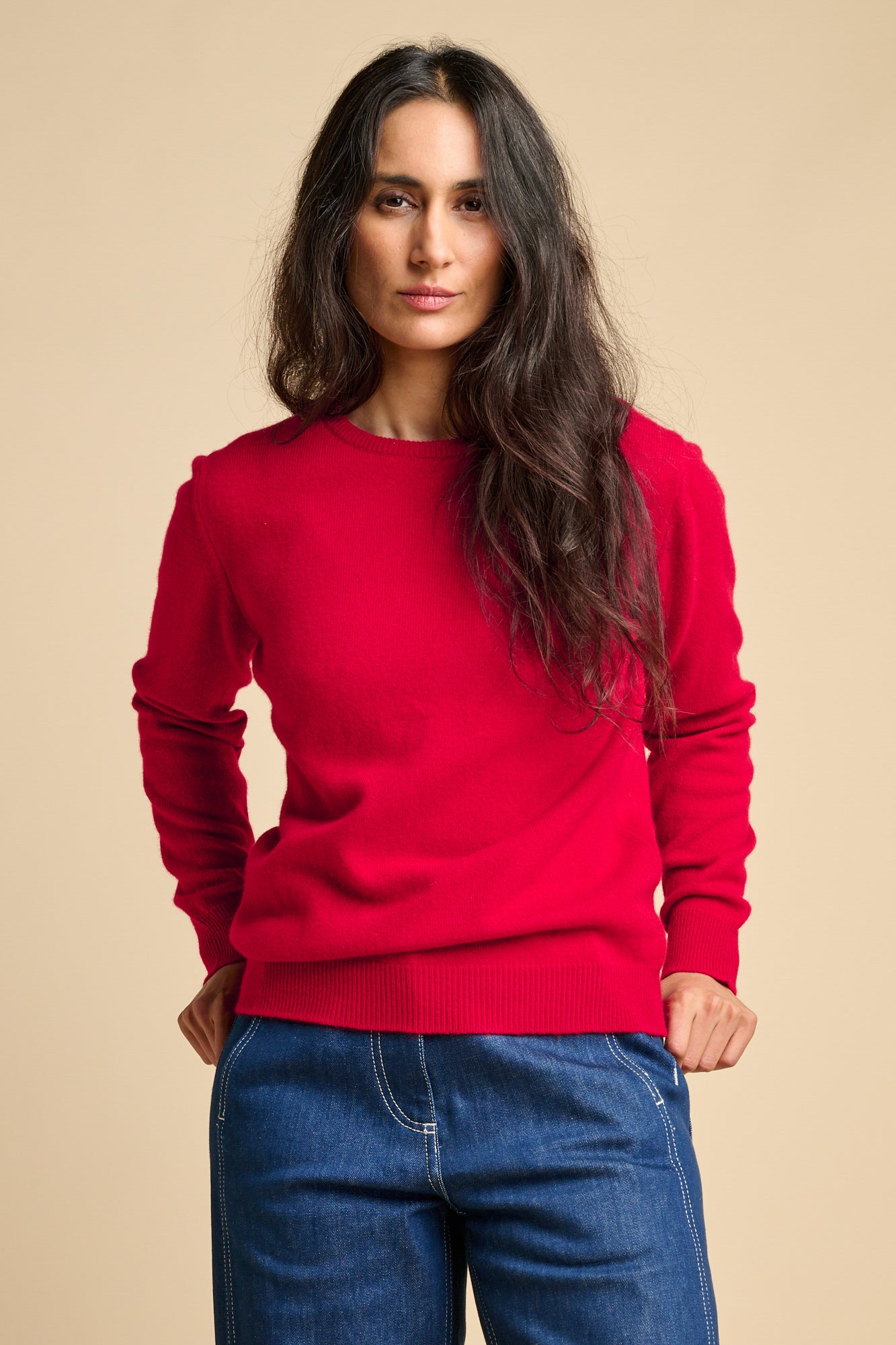 A woman wearing lambswool crew neck jumper in red paired with blue. 
