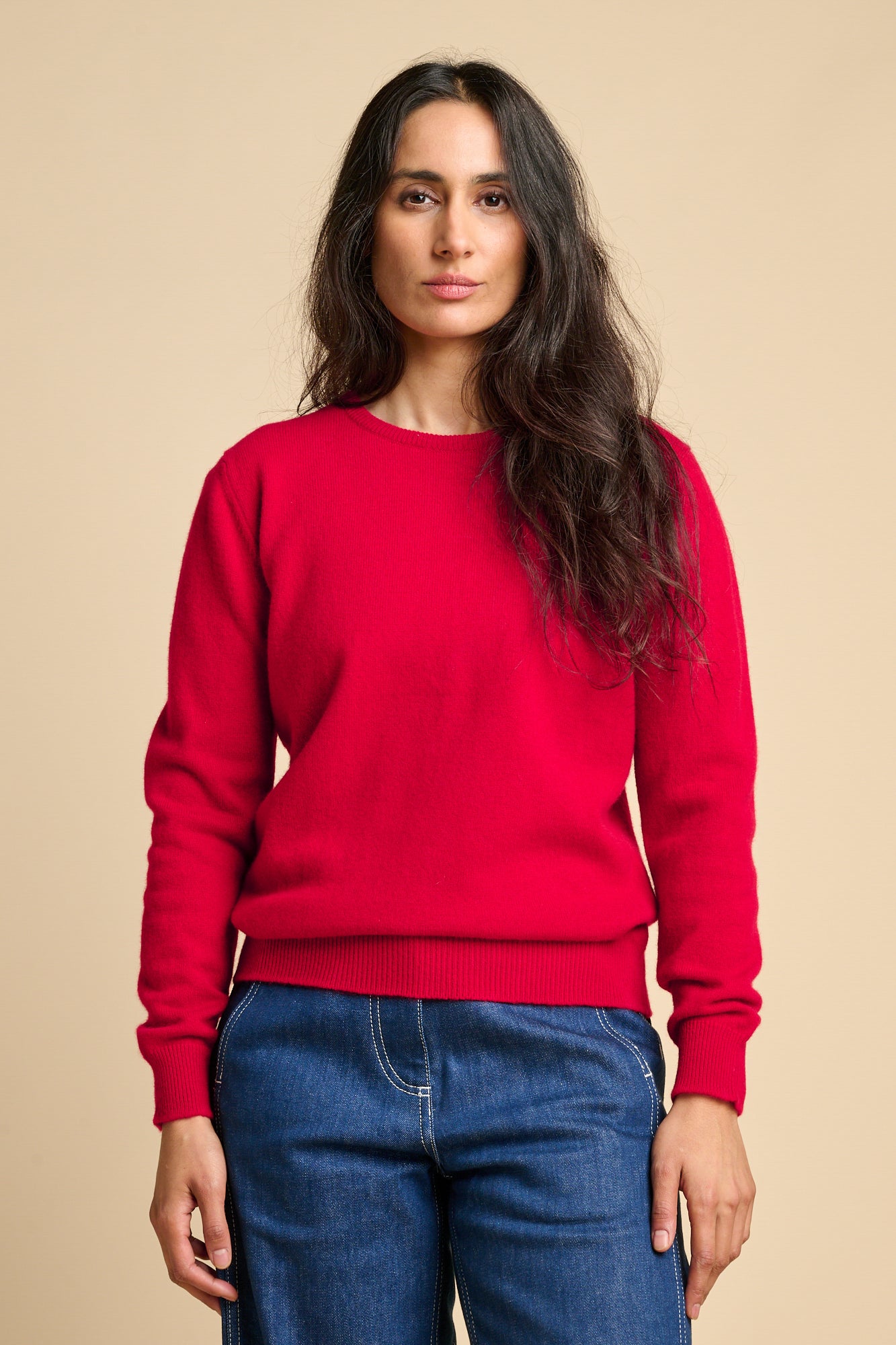 A woman wearing lambswool crew neck jumper in red paired with blue. 