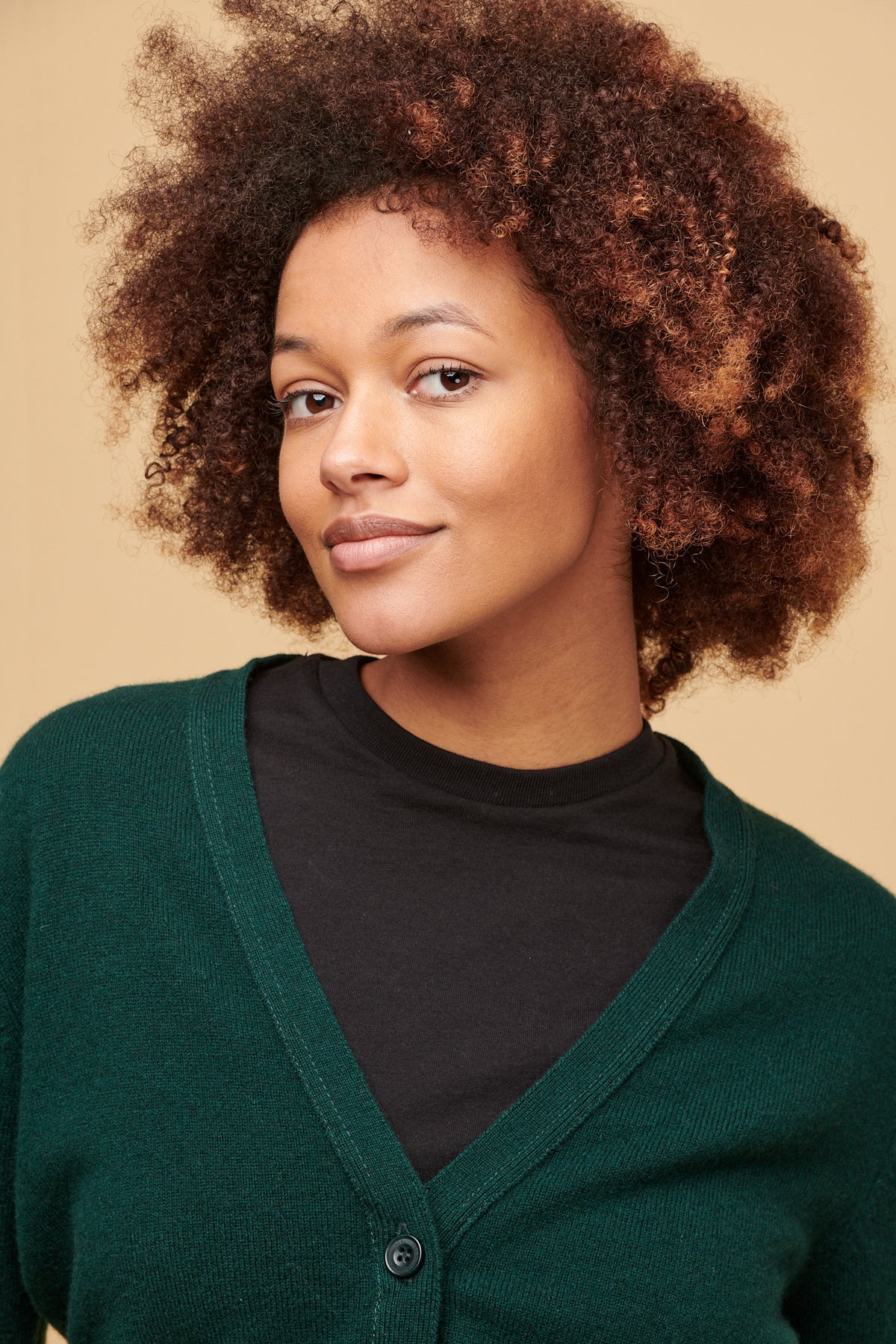 
            Portrait of femalewith curley brown hair wearing black t shirt with v neck cardigan in bottle green over the top