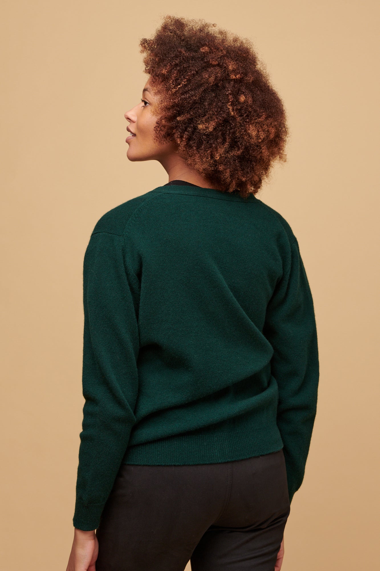 Thigh up of the back of female wearing bottle green cardigan paired with chinos