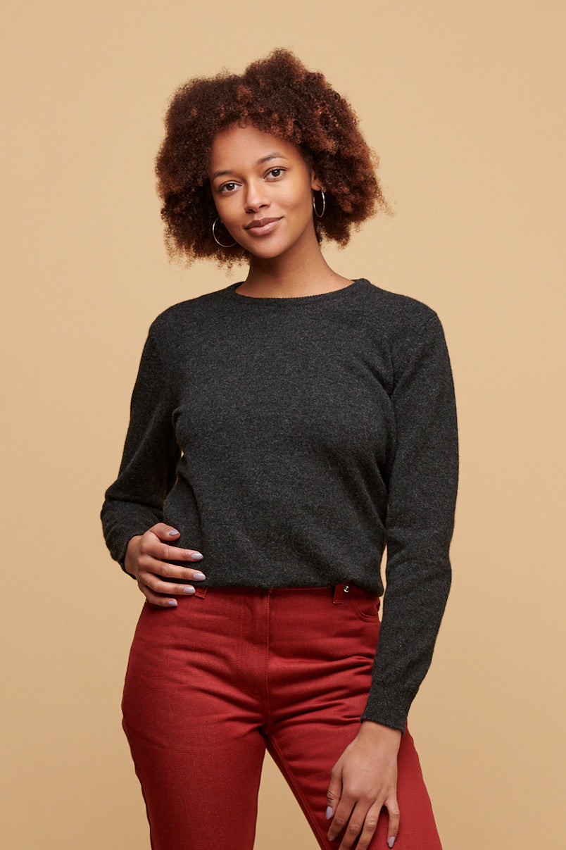 Thigh up of black female with afro wearing women's lambswool crew neck jumper in charcoal paired with women's Gloria jeans in burgundy