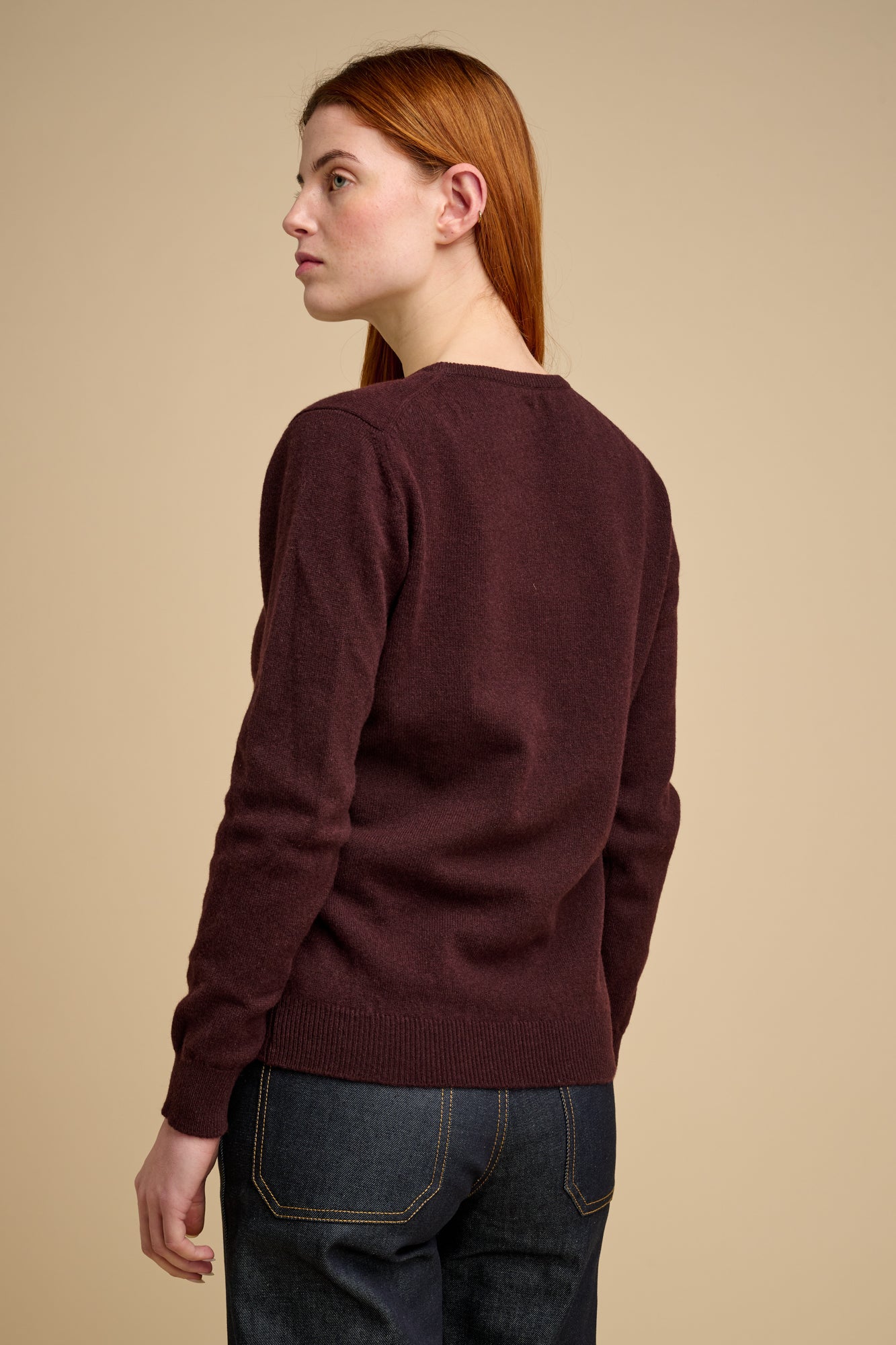 The back of woman wearing lambswool crew neck jumper in chocolate.