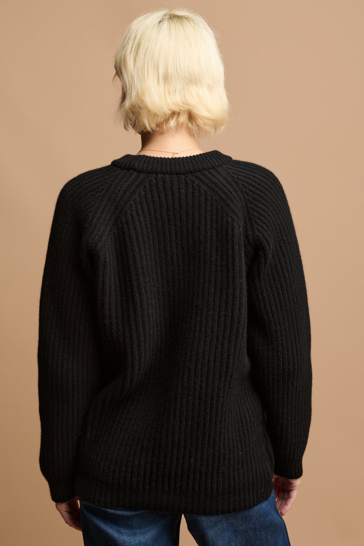 
            The back of female with blonde hair wearing lambswool fisherman ribbed jumper in black