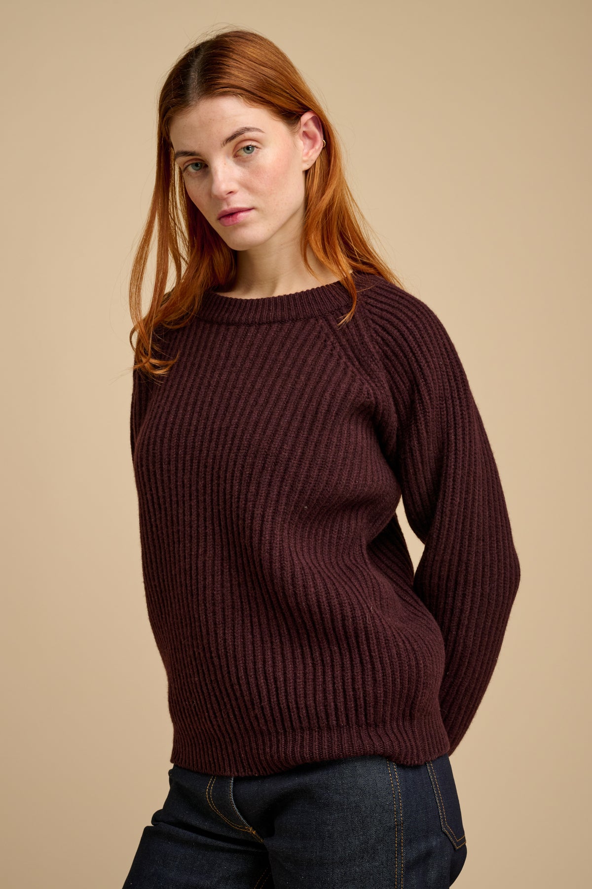 Woman wearing a lambswool fisherman ribbed jumper in chocolate against a beige background.