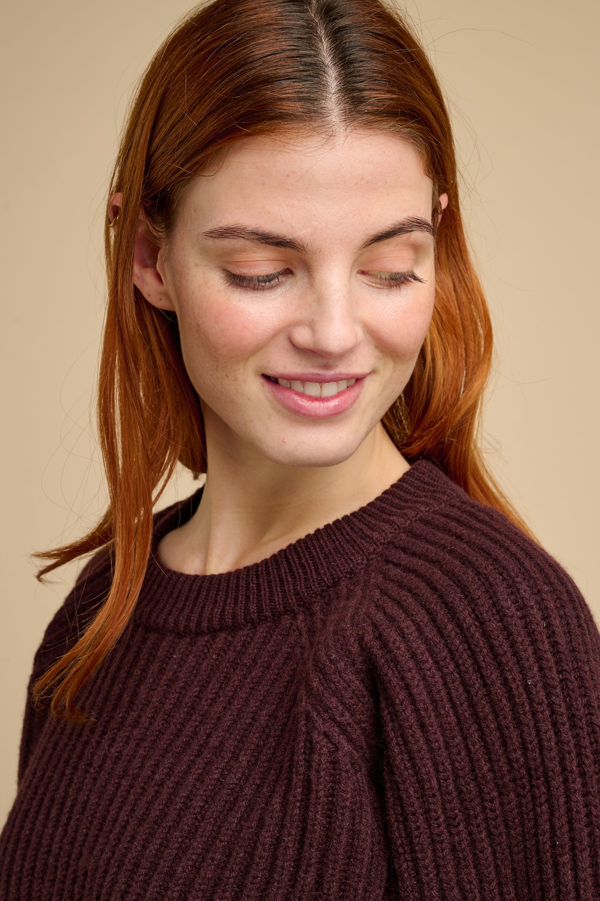 Woman wearing a lambswool fisherman ribbed jumper in chocolate against a beige background.