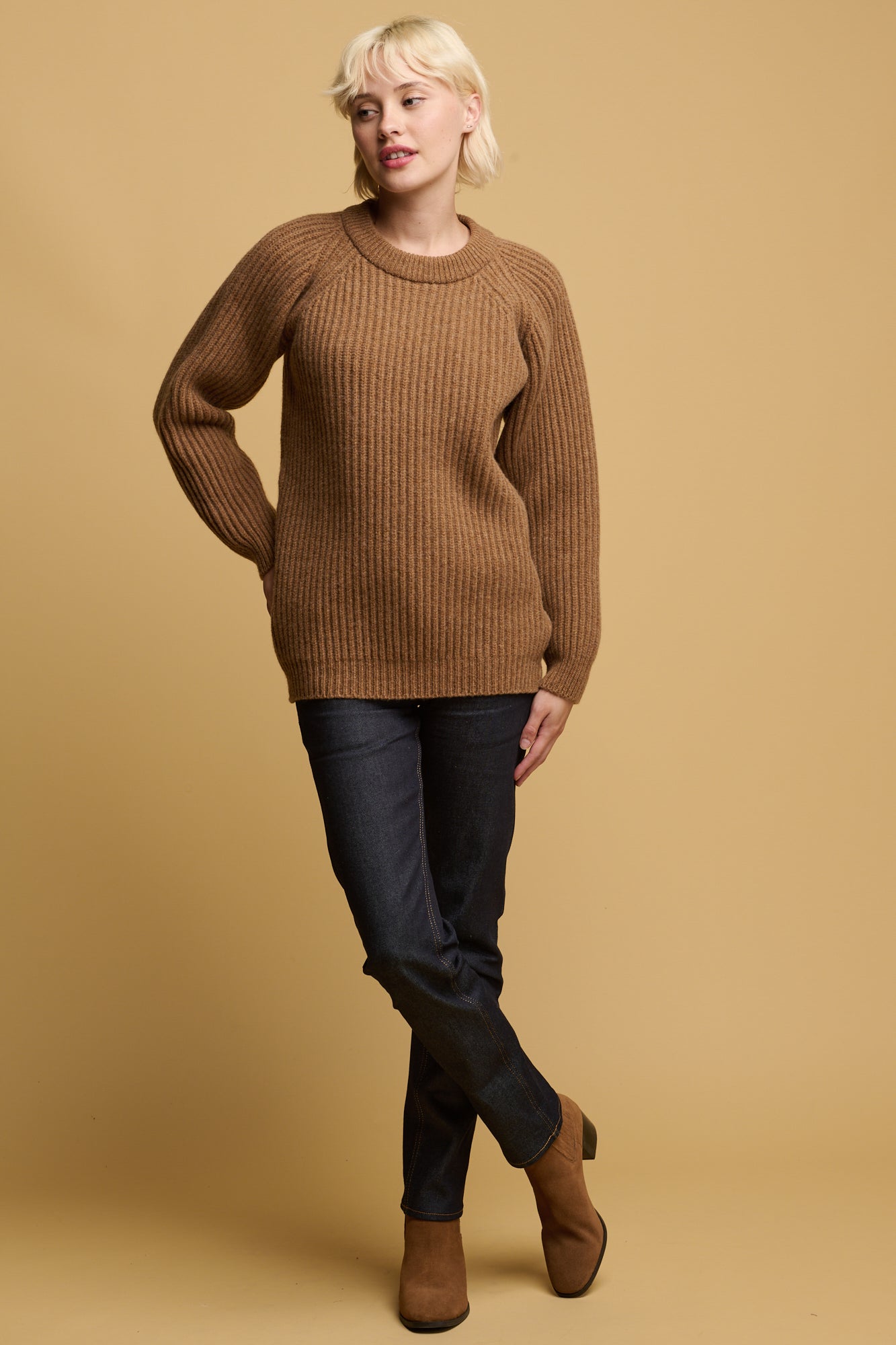 female wearing lambswool fisherman ribbed jumper in dark camel paired with straight leg jeans in indigo and dark camel coloured suede boots