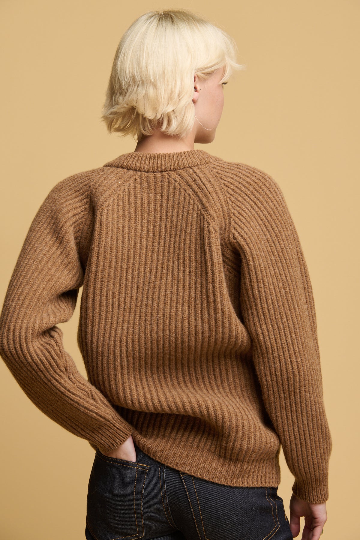 
            The back of female wearing lambswool fisherman ribbed jumper in dark camel 