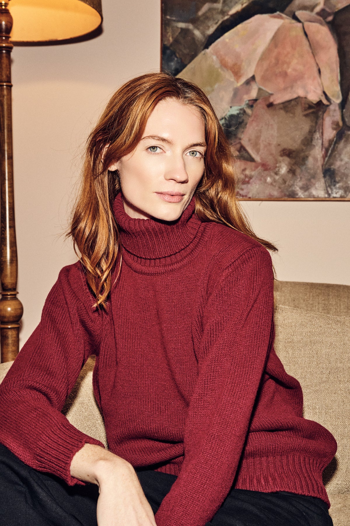 Woman wearing a burgundy sweater sitting on a couch in a cozy room.