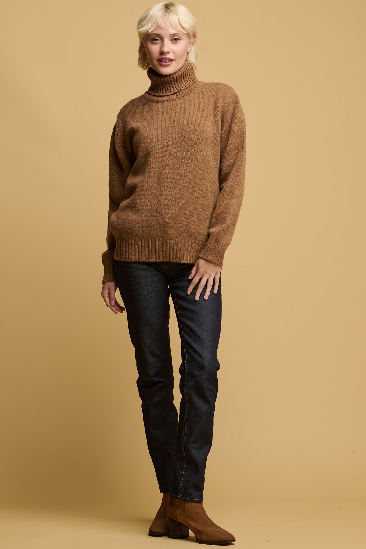 
            Female wearing lambswool roll neck in dark camel paired with high rise straight leg jeans in indigo and dark camel boots 