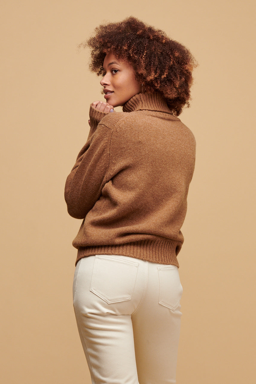 Thigh up of the back of female wearing lambswool roll neck in dark camel paired with Gloria jeans in ecru