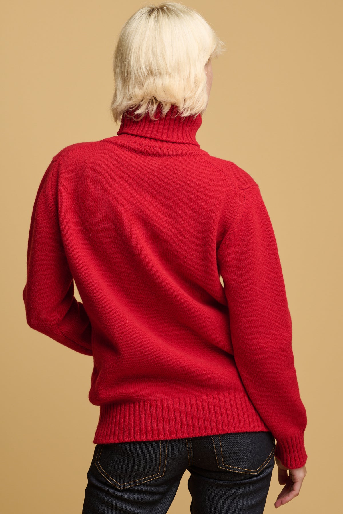The back of blonde female wearing lambswool roll neck jumper in red