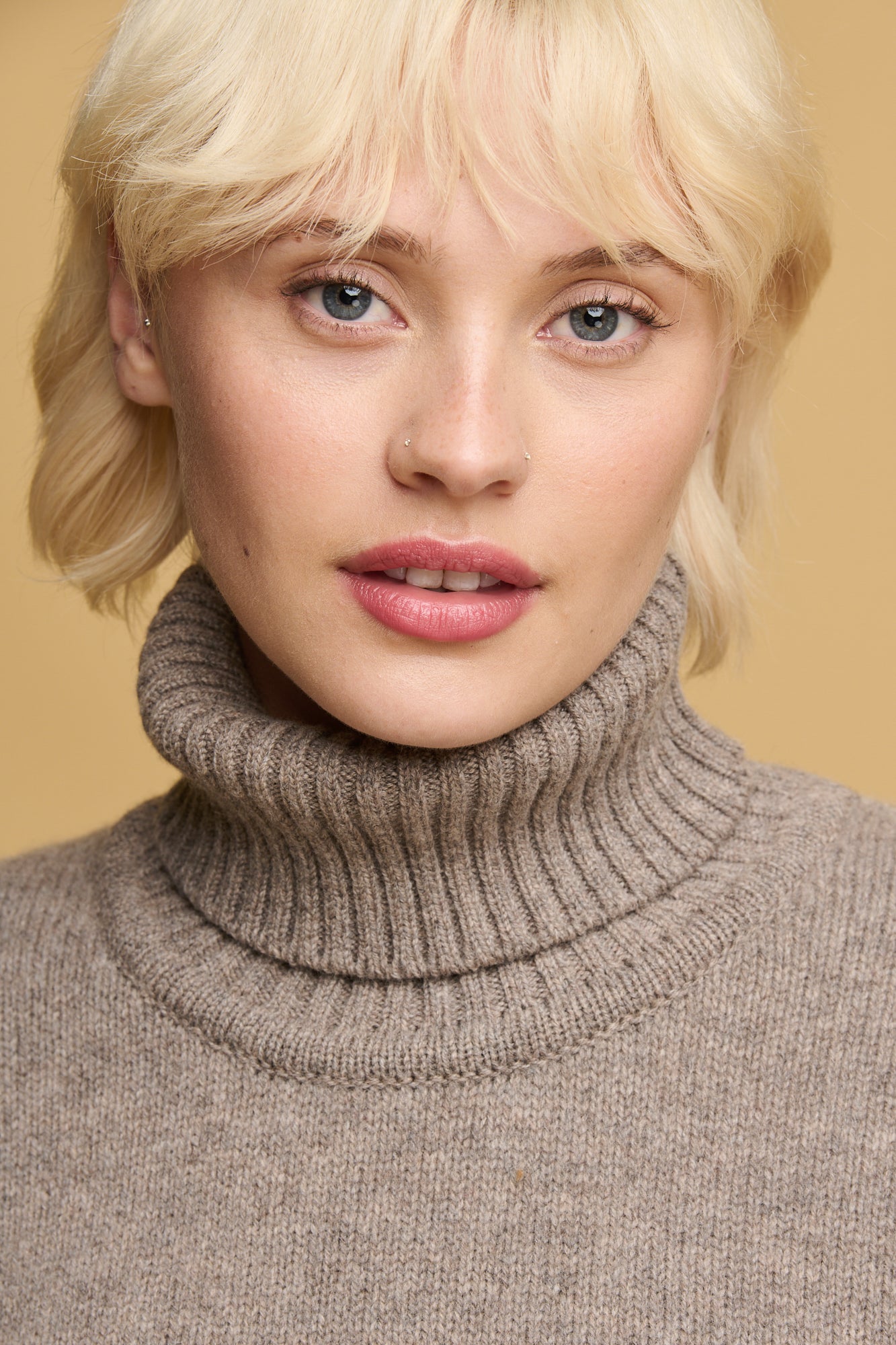 Portrait of female with blonde hair and blue eyes wearing lambswool roll neck in truffle