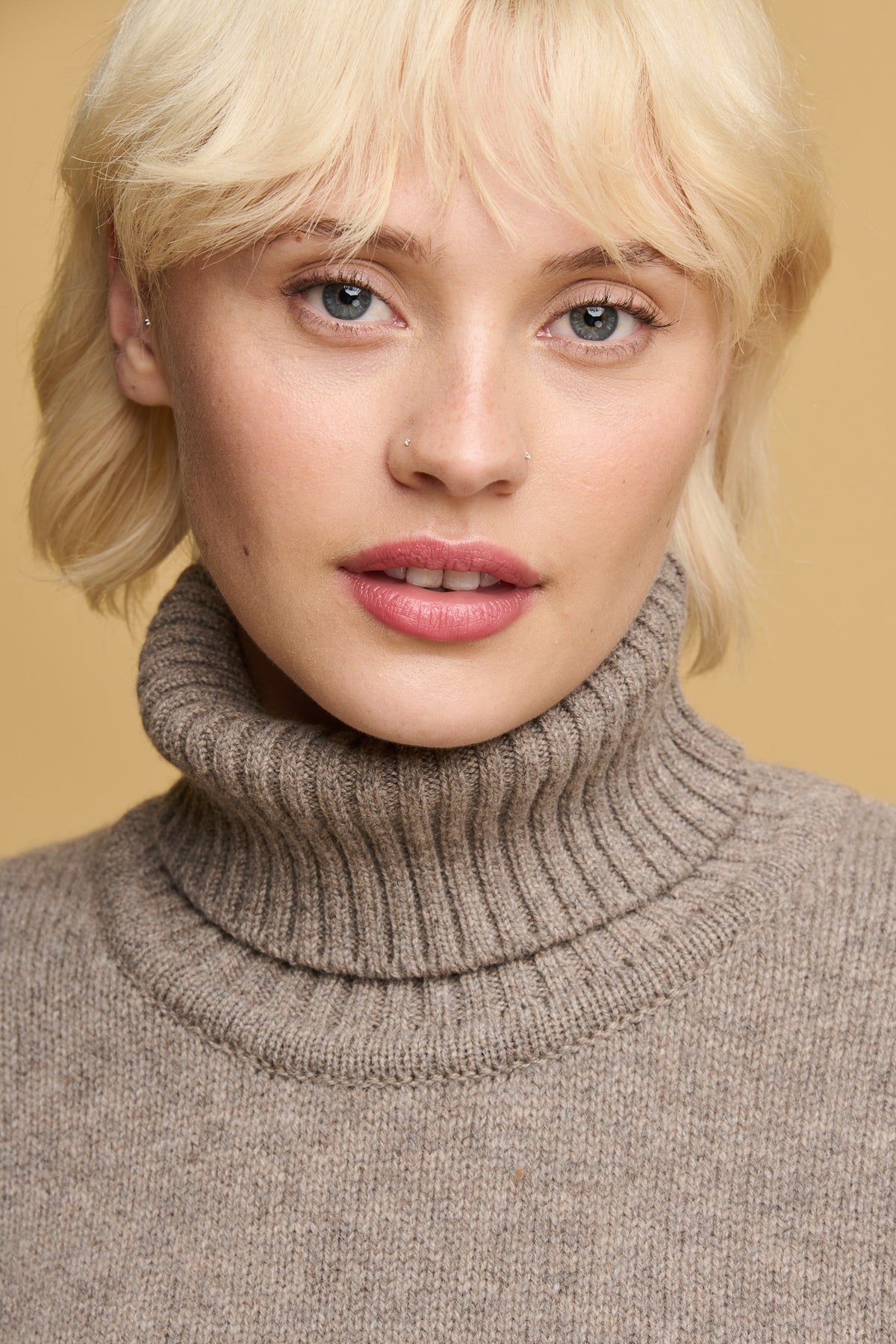 
            Portrait of female with blonde hair and blue eyes wearing lambswool roll neck in truffle