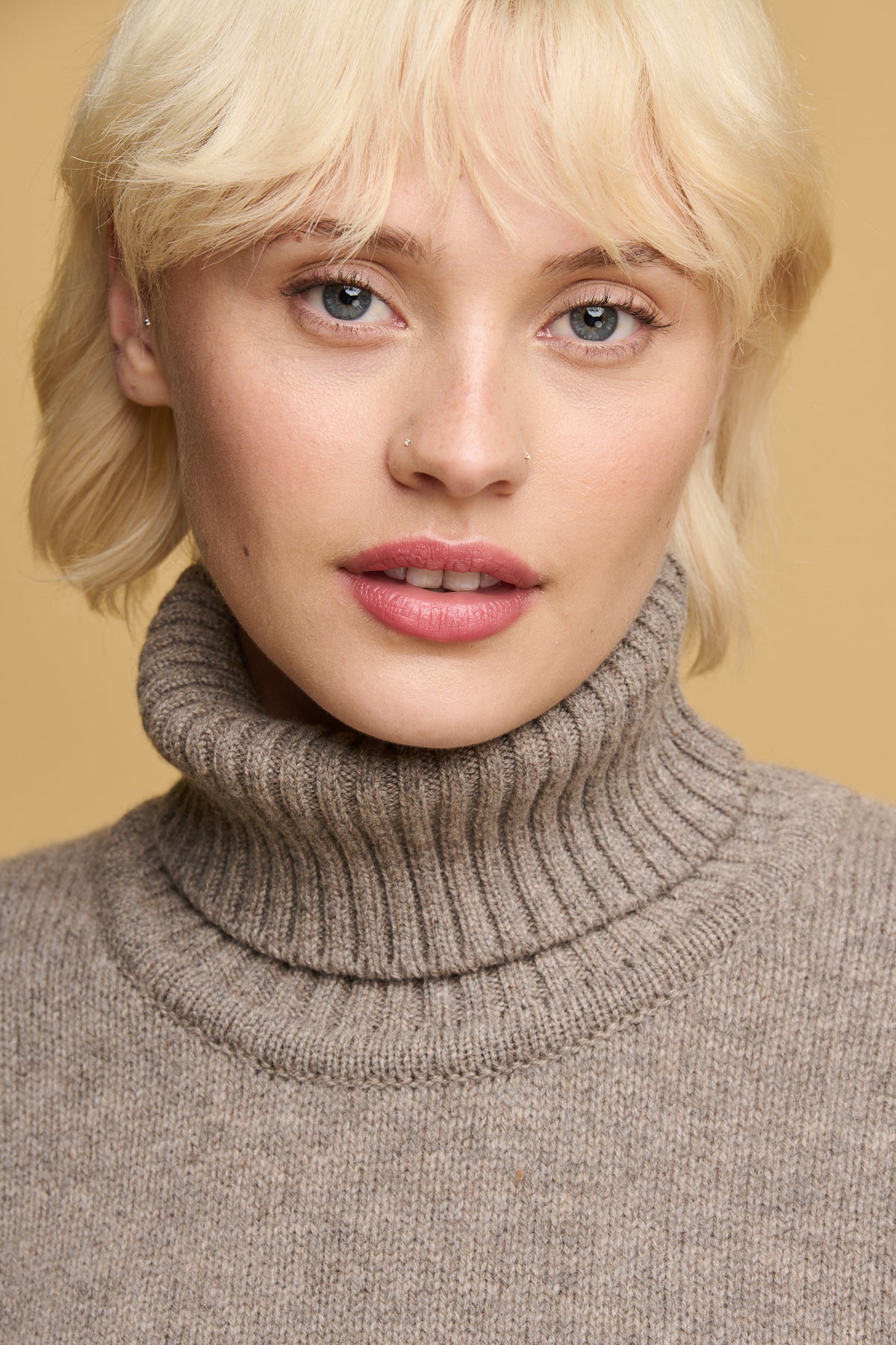 Portrait of female with blonde hair and blue eyes wearing lambswool roll neck in truffle
