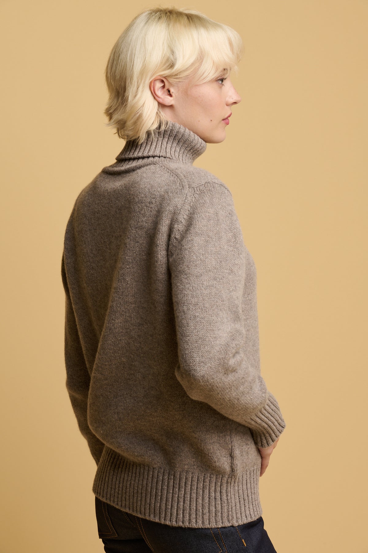 The back of female with blonde hair wearing lambswool roll neck in truffle
