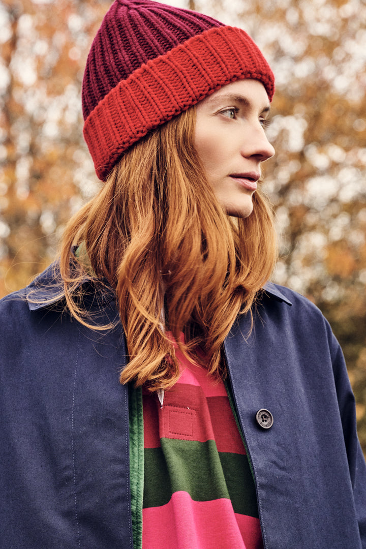 Person wearing a red knit beanie and colorful striped sweater with a blurred autumn background