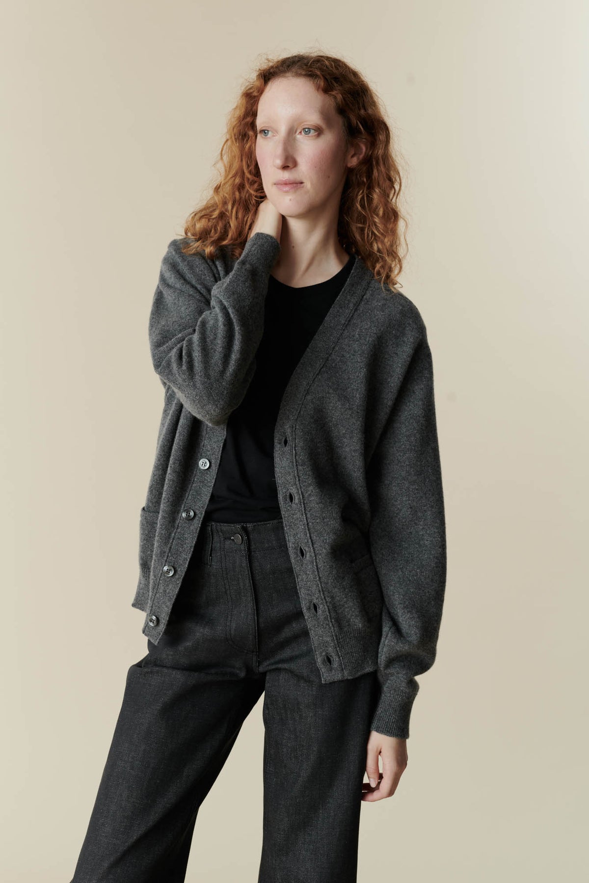 Image of fair skinned female with curly ginger hair wearing v neck cardigan in charcoal over black t shirt