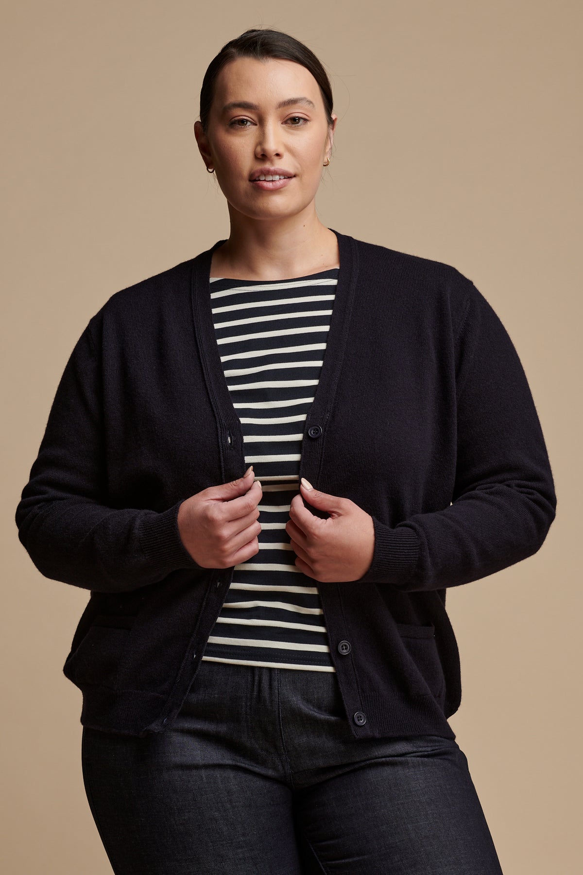 Thigh up image of female wearing lambswool v neck cardigan in navy unbuttoned over Breton top in navy-ecru, paired with work trousers in indigo.