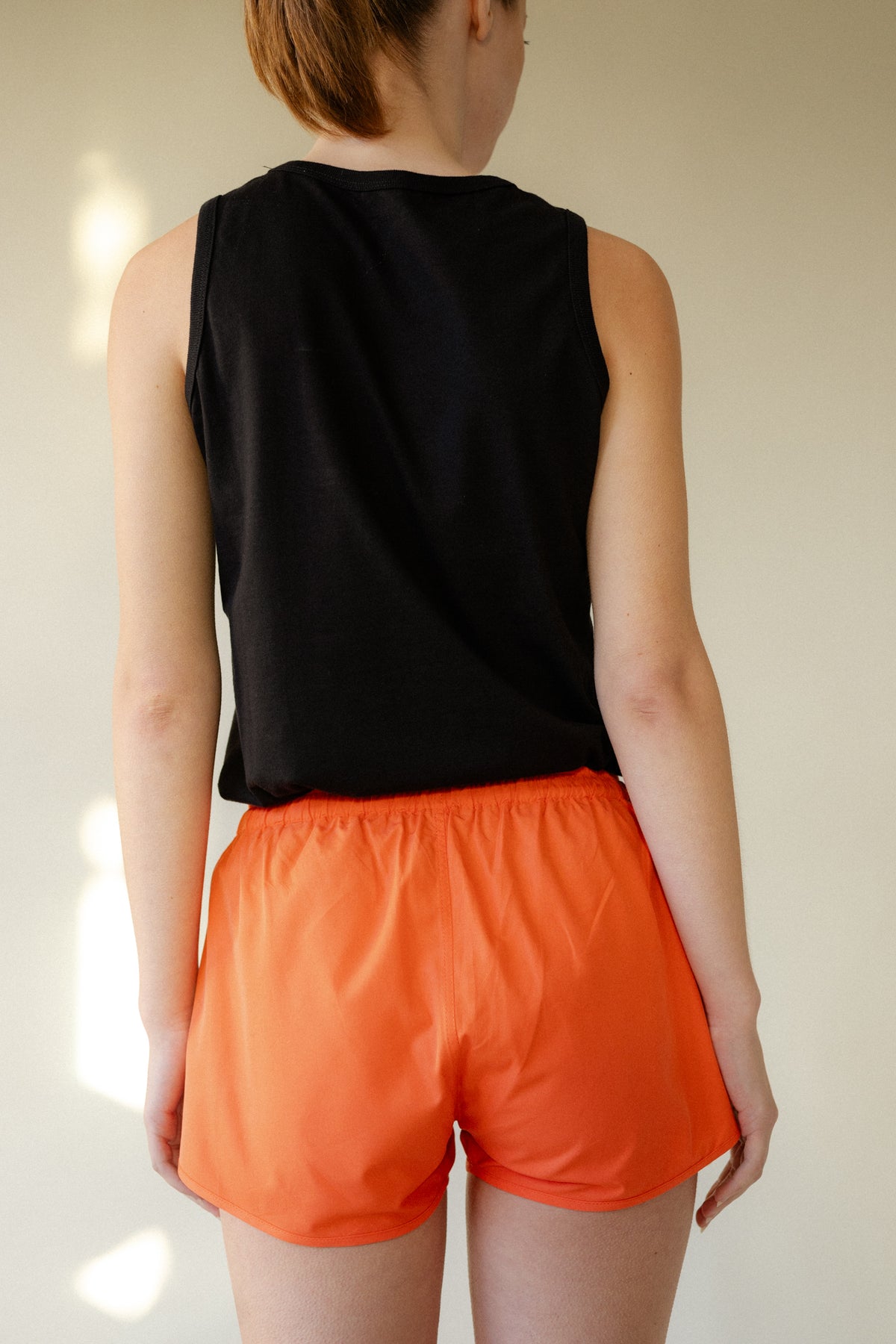 shot of female back of head to thigh wearing lightweight running shorts plastic free flame red.