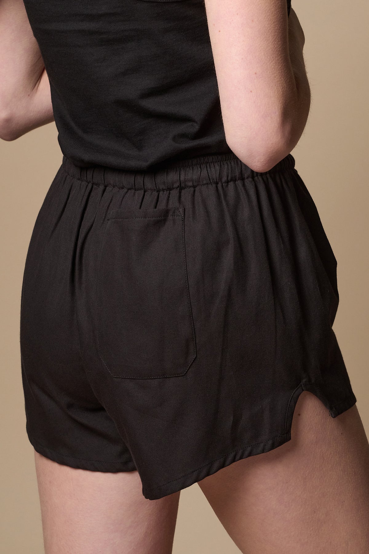 Back of female wearing lightweight sports short plastic free in black with back pocket on right leg