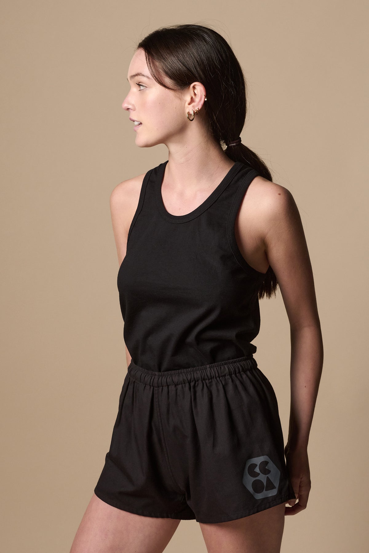 Thigh up image of female wearing lightweight sports short plastic free in black with CCOA logo on left leg