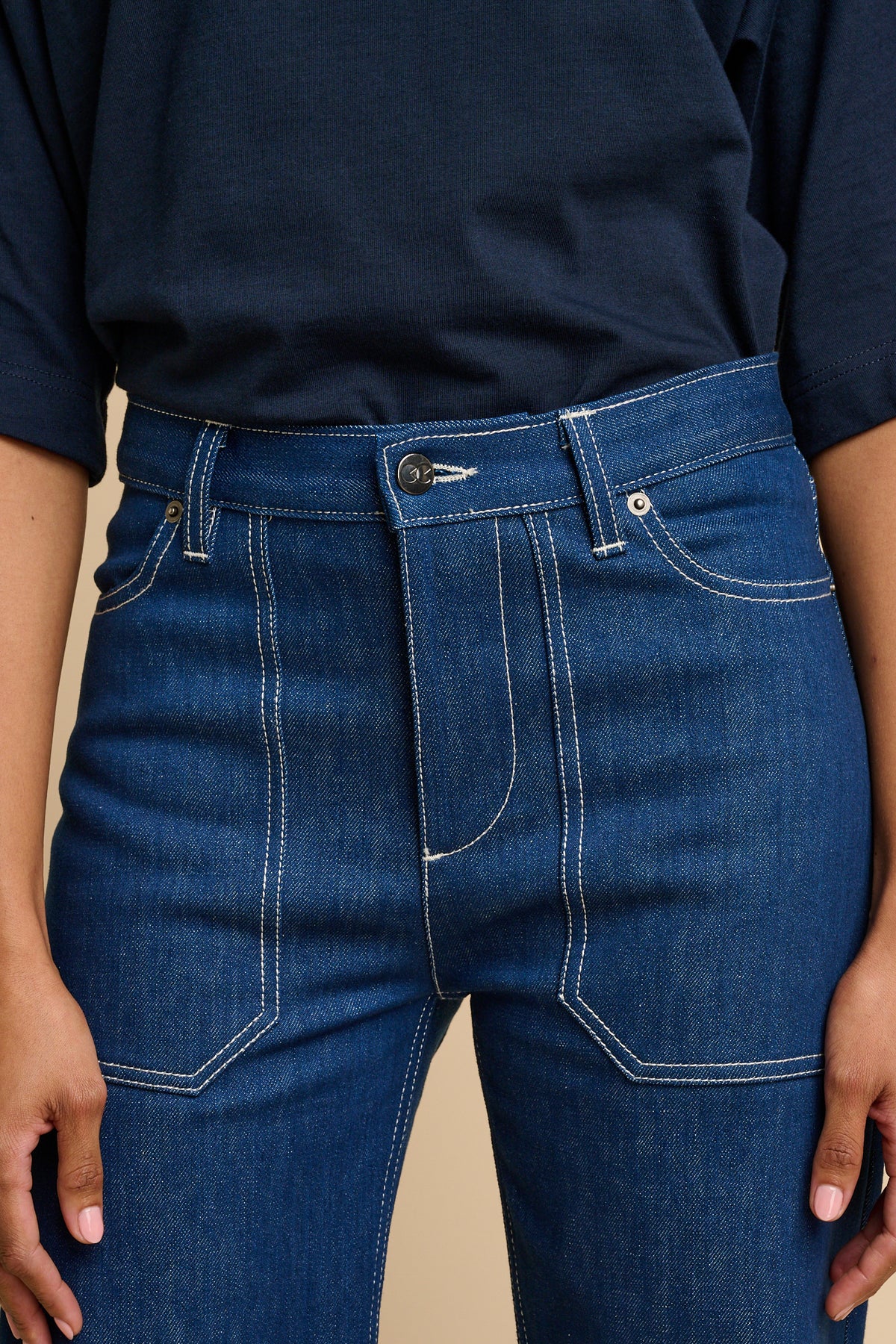 Woman wearing a navy t-shirt and blue jeans against a beige background.