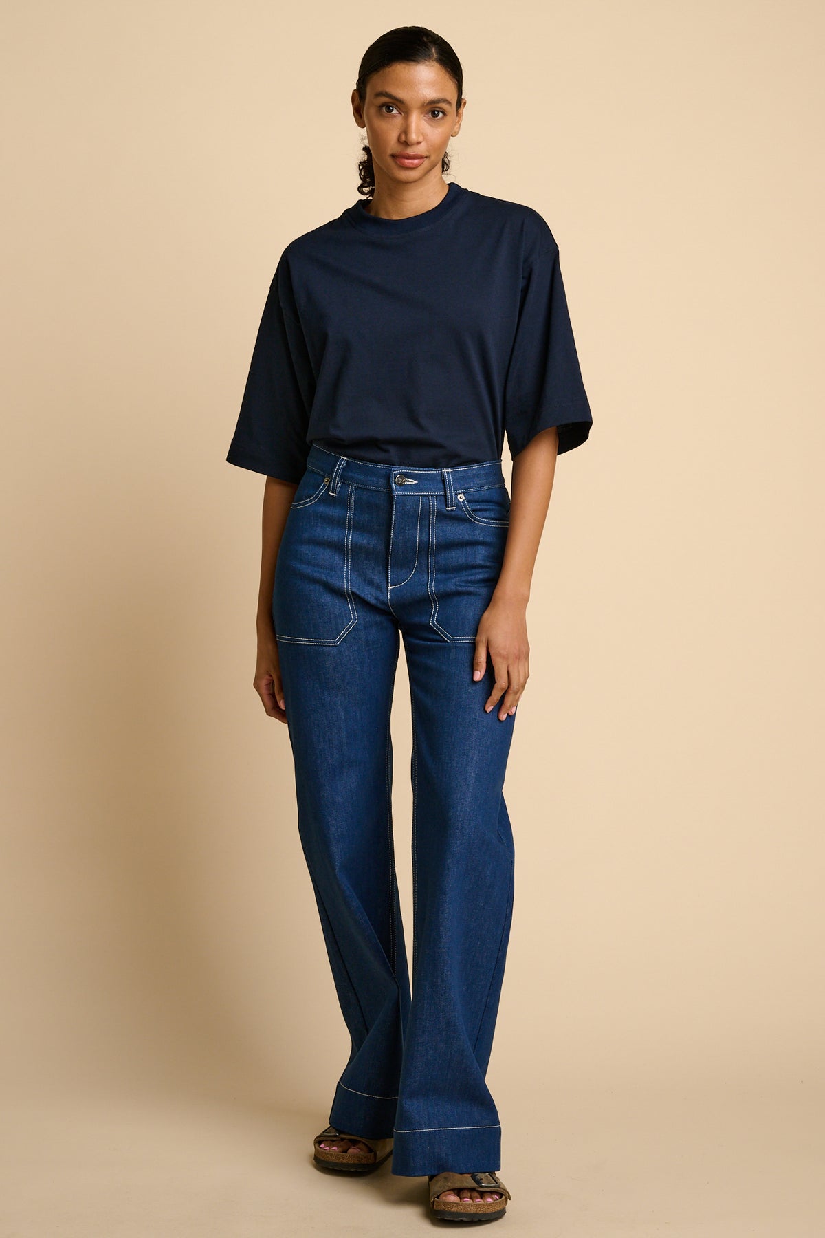 Woman wearing a navy t-shirt and blue jeans against a beige background.