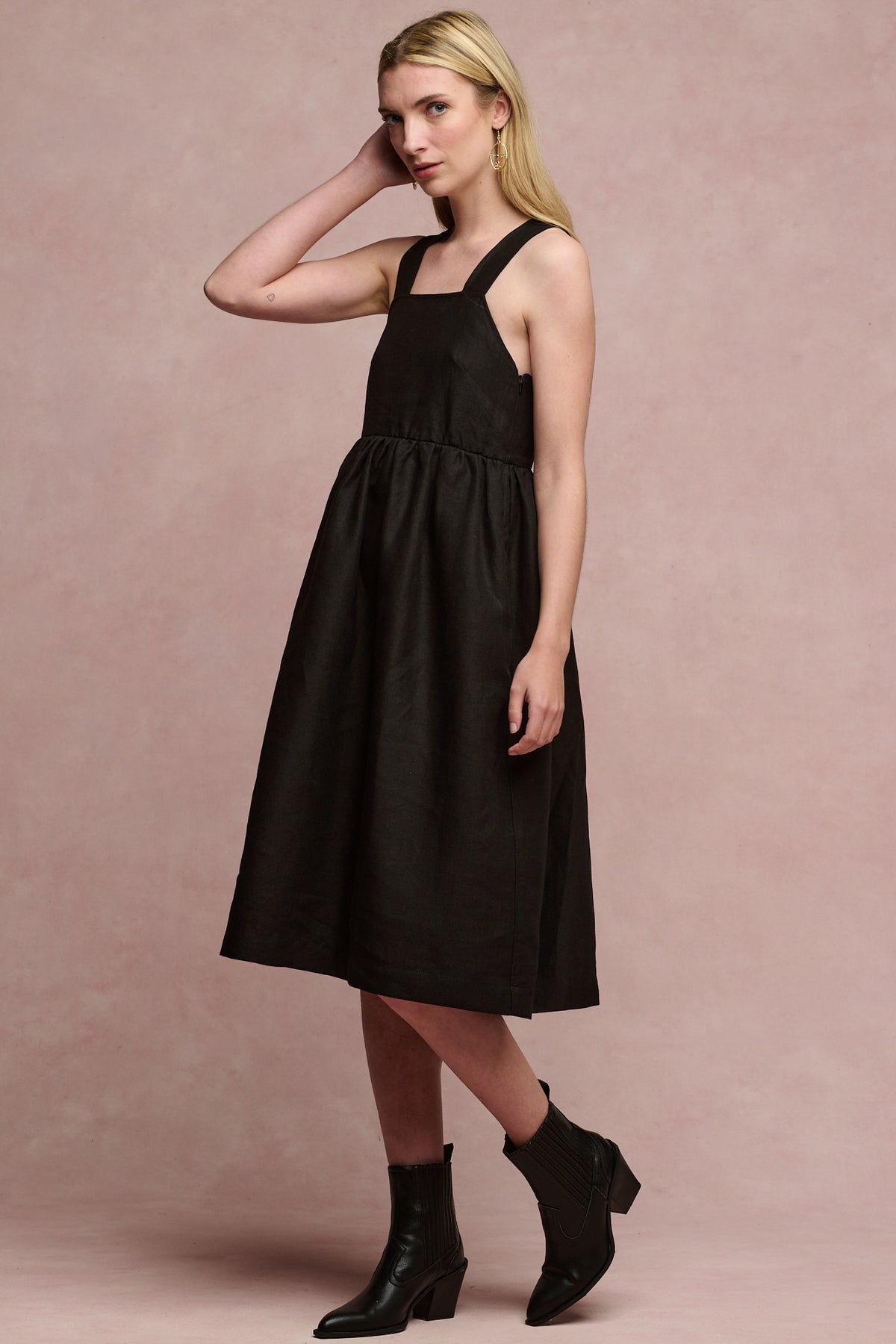 
            Full body image of fair skinned, blonde female wearing linen sun dress in black paired with black heeled boots