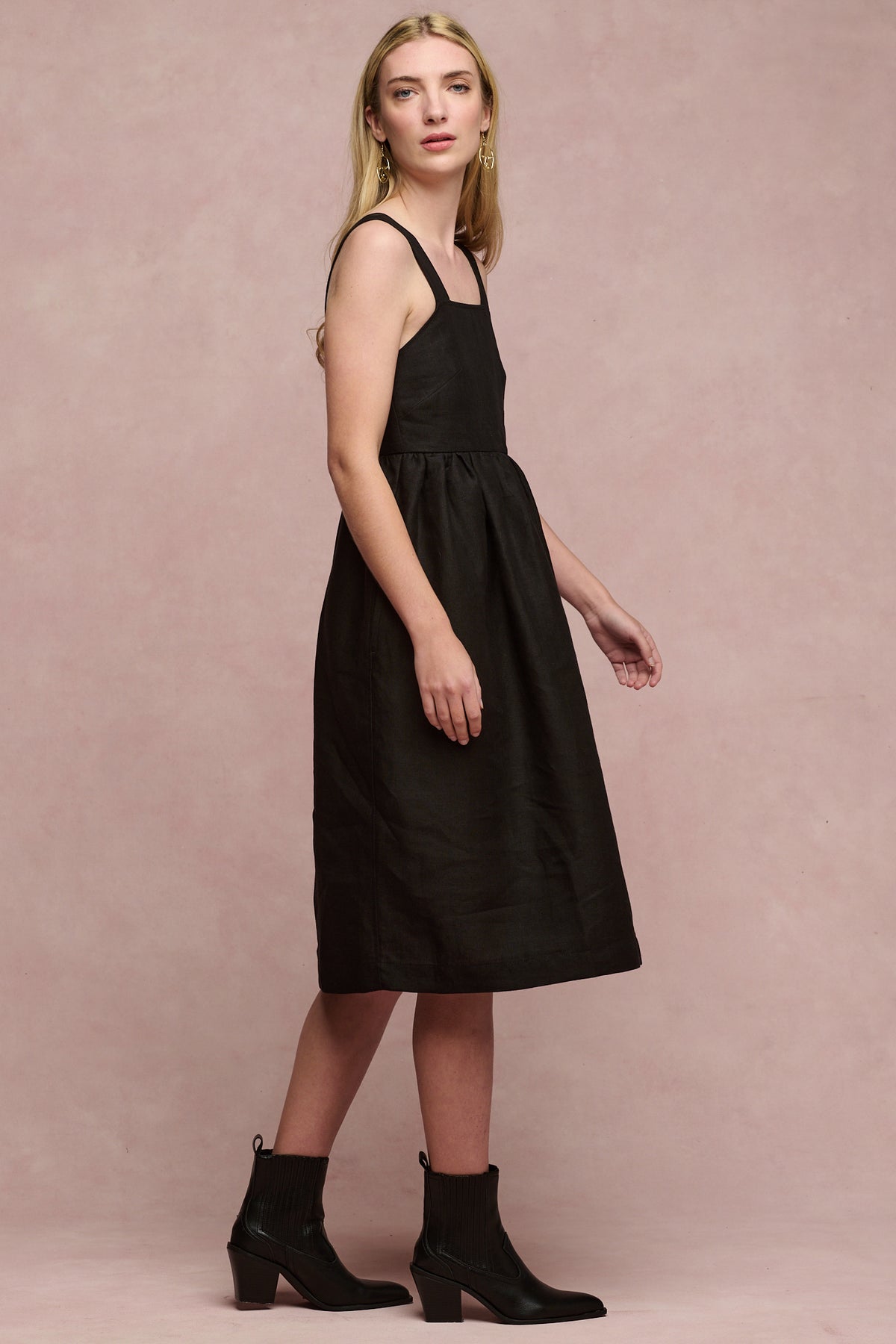 Full body image of female wearing linen sun dress in black paired with black heeled boots