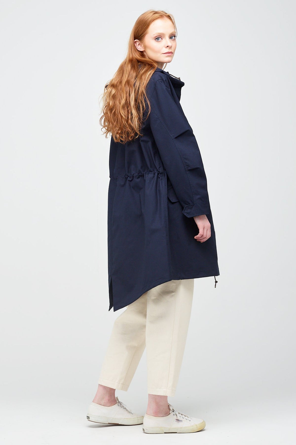 
            Rear shot of A young, white female model with ginger hair wearing a long navy parka unzipped. The parka is styled with a navy striped breton top &amp; ecru jeans.