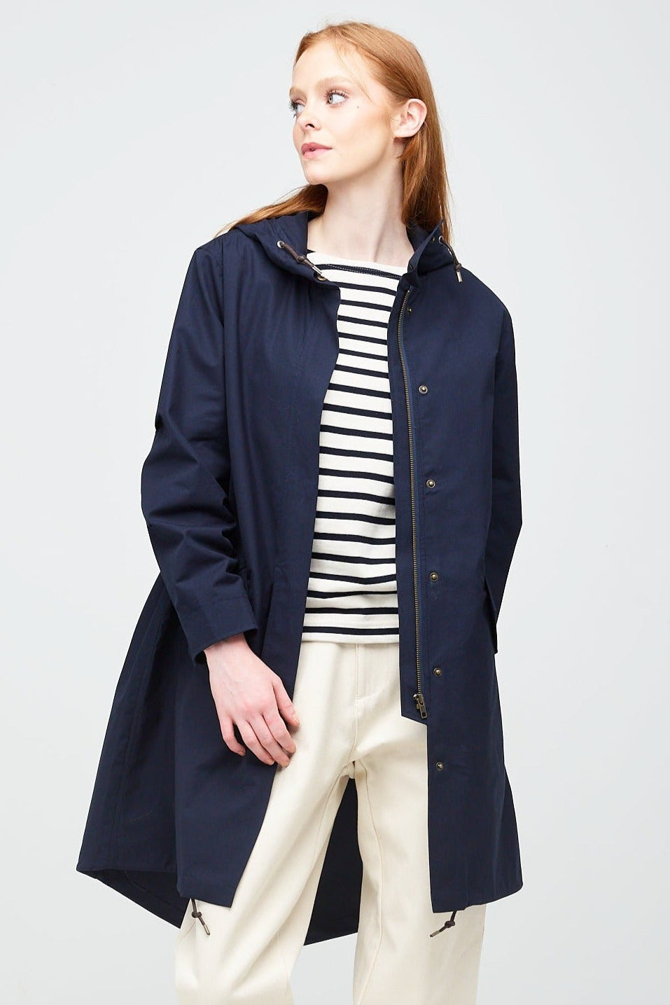 
            A young, white female model with ginger hair looking to the left wearing a long navy parka unzipped. The parka is styled with a navy striped breton top &amp; ecru jeans.