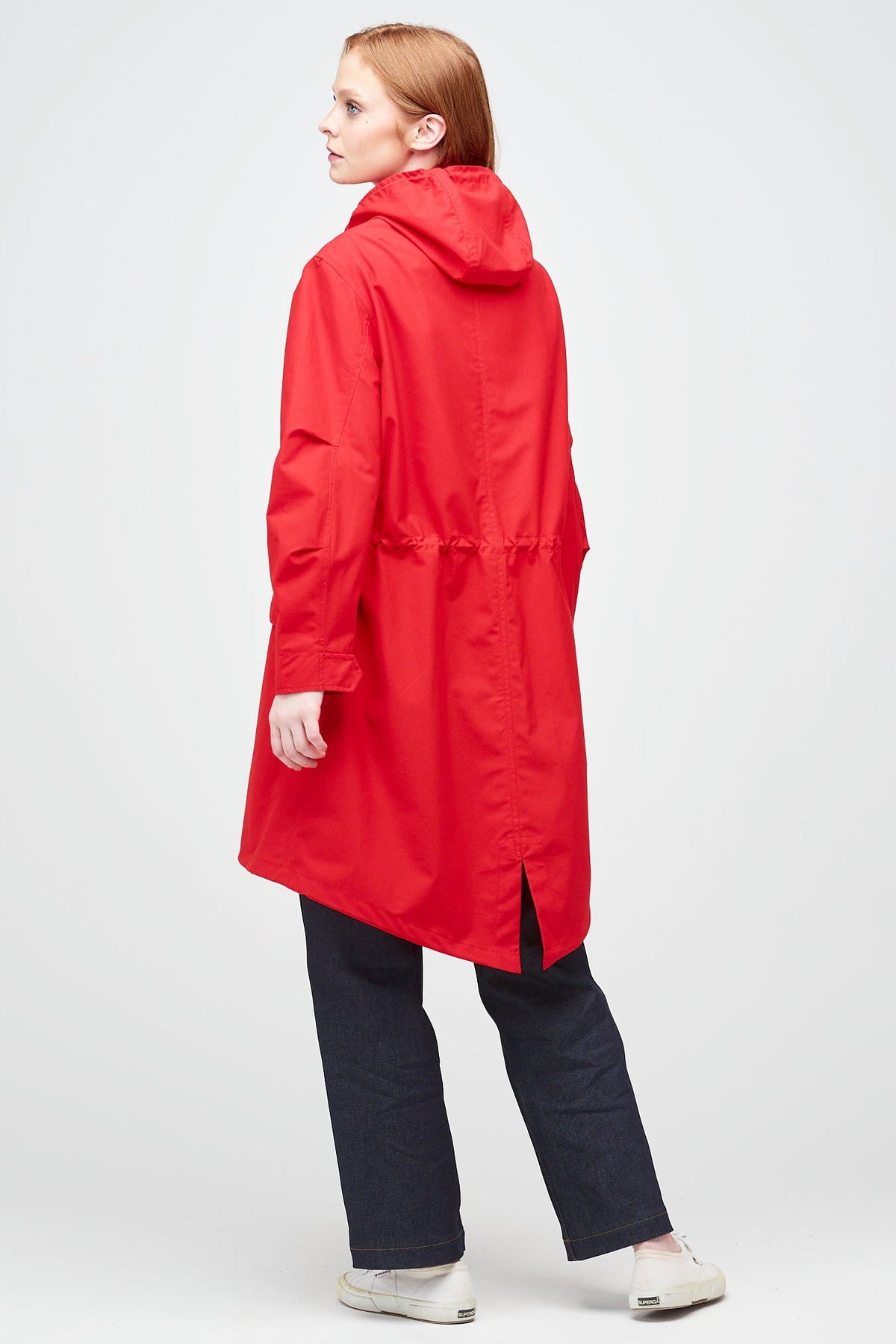 
            rear shot of A young, white female model with ginger hair wearing long red parka. The parka is styled with indigo jeans and a white trainer.