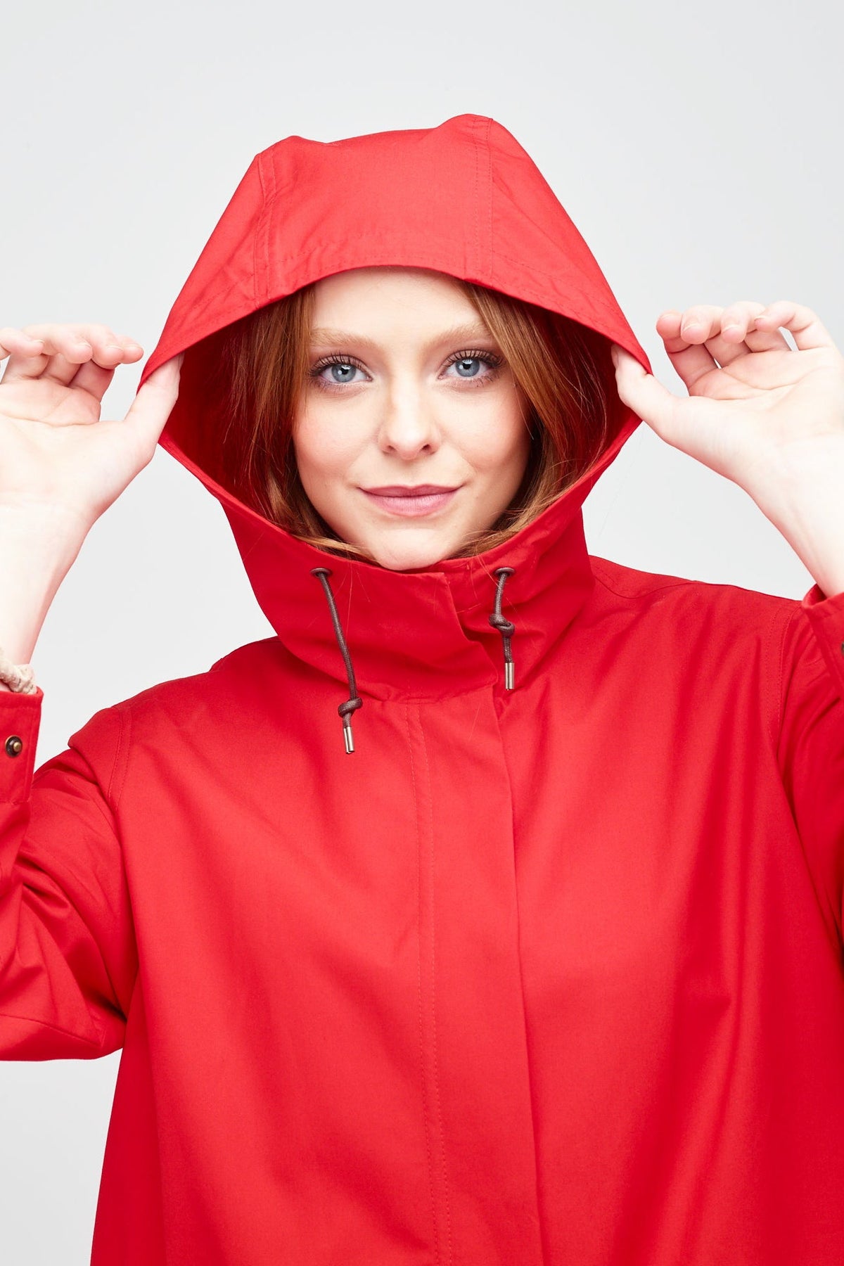 
            shoulders up image of a young, white model with ginger hear wearing a red long parka with the hood up