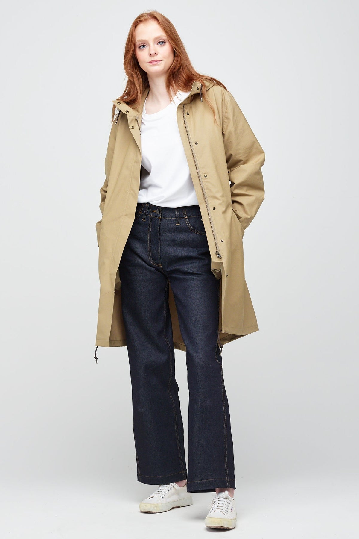 
            Front shot of a young, white female model with ginger hair wearing long stone coloured parka. The parka is styled with indigo jeans and a white trainer.