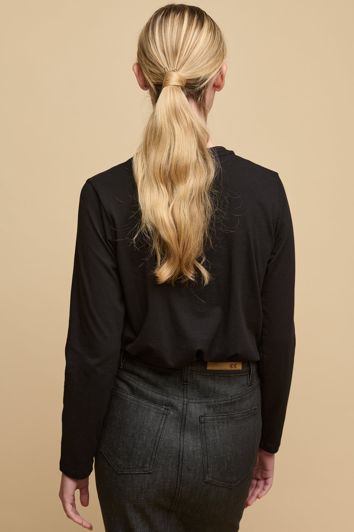 
            Back of female with long blonde hair wearing long sleeve t-shirt in black tucked into Charlie denim maxi skirt