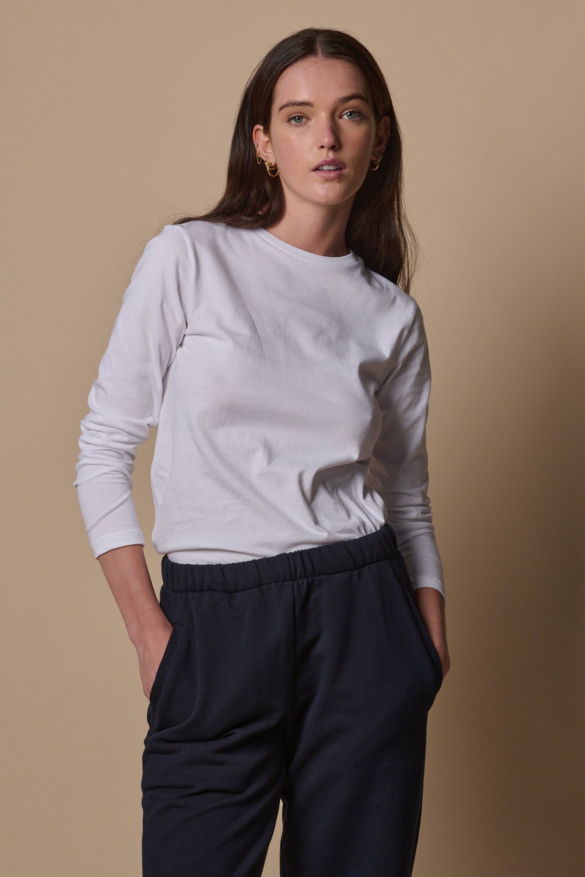 
            Thigh up image of brunette female wearing long sleeve t shirt in white tucked in navy sweatpants with sleeves pushed up to the arms