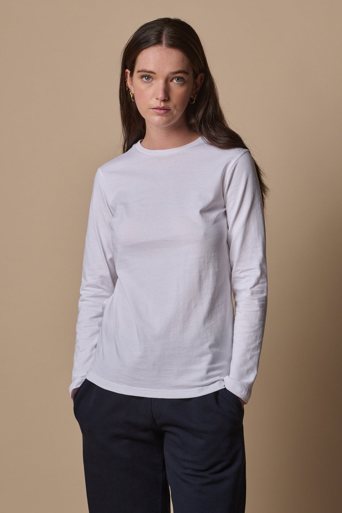 Brunette female wearing long sleeve t shirt in white with hands in pockets of navy sweatspants