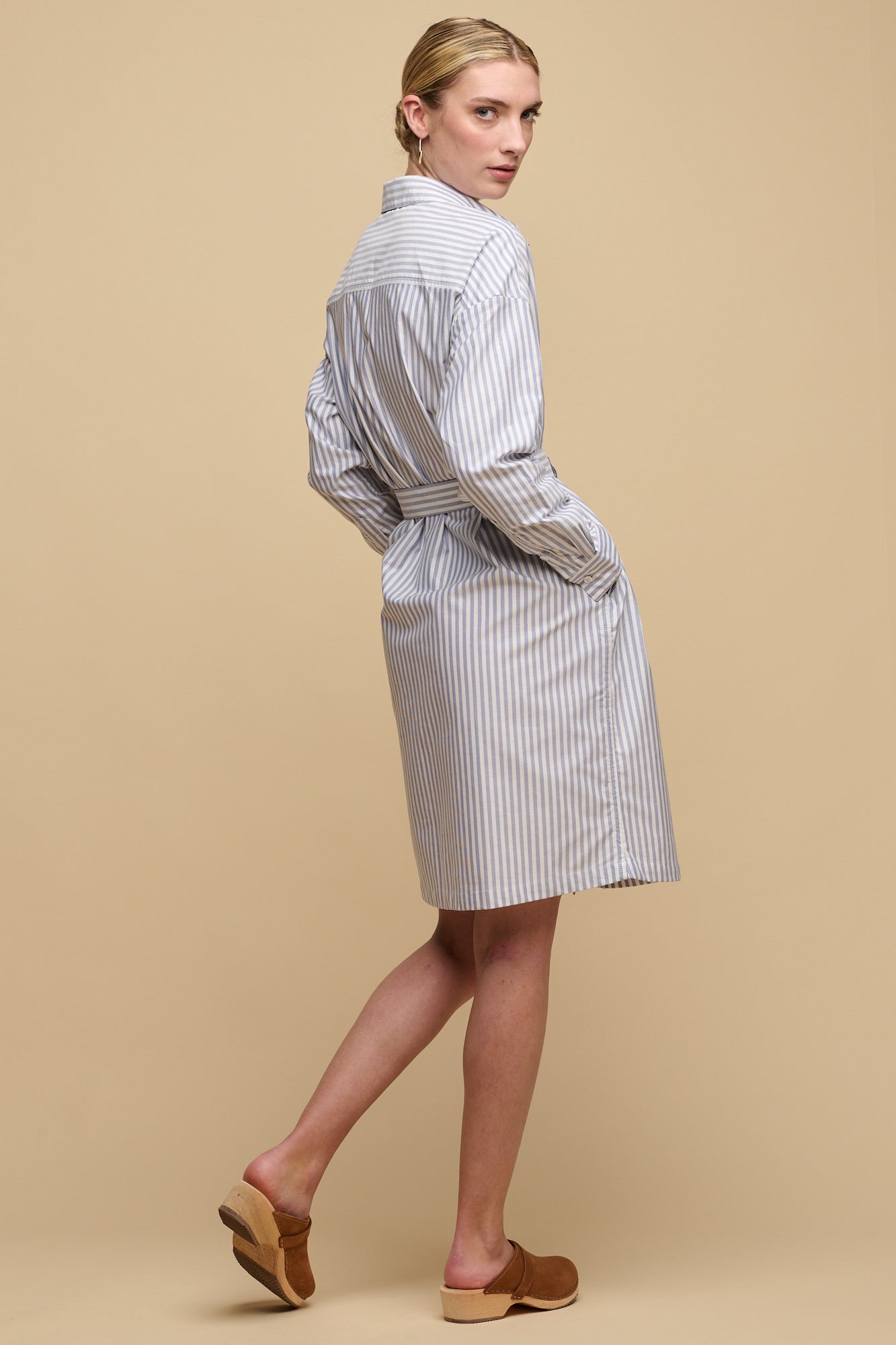 Full body image of the back of women's Lorelle belted midi cotton shirt dress in blue and white stripes with hands in pockets