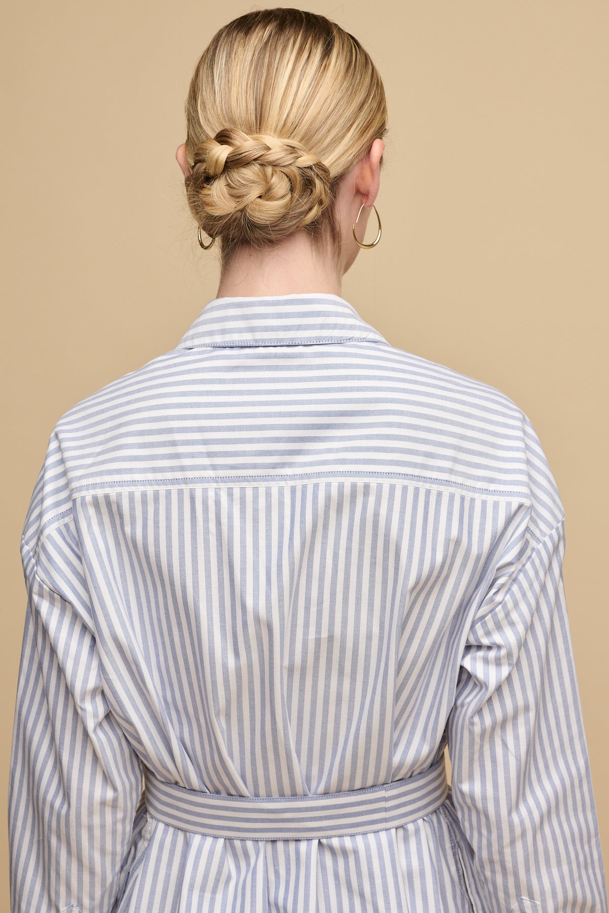 waist up image of the back of white female with blonde hair tied back into low bun wearing belted midi cotton shirt dress in white blue stripes