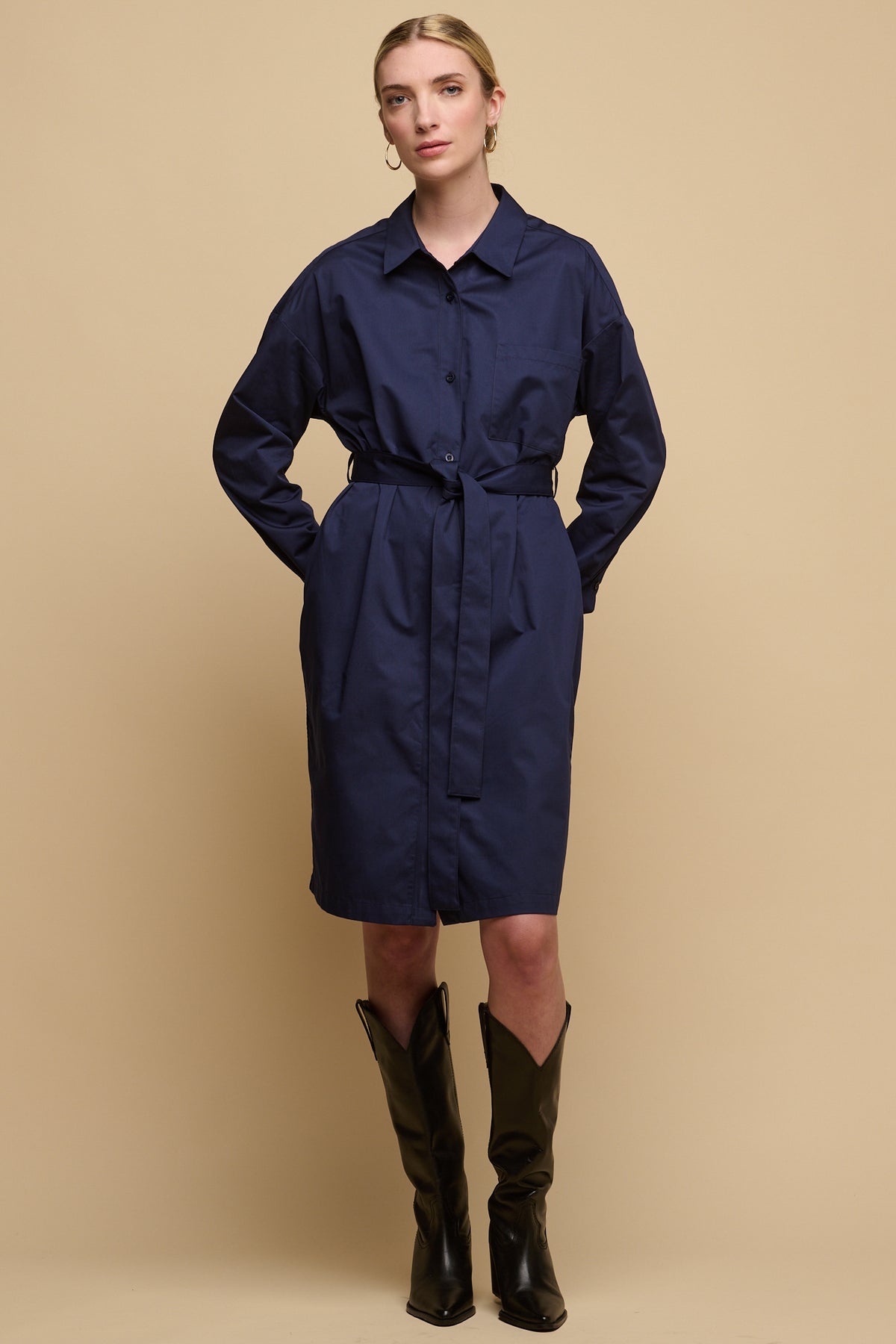 Full body image of female with blonde hair tied up wearing Lorelle belted midi cotton shirt dress in navy, worn with thigh high black boots