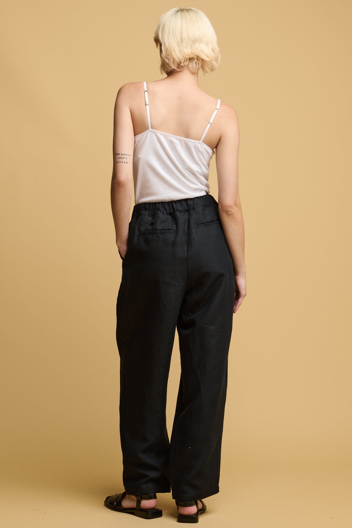 The back of female wearing lorna elasticated waist linen trousers with two back jet pockets, worn with white camisole tucked in