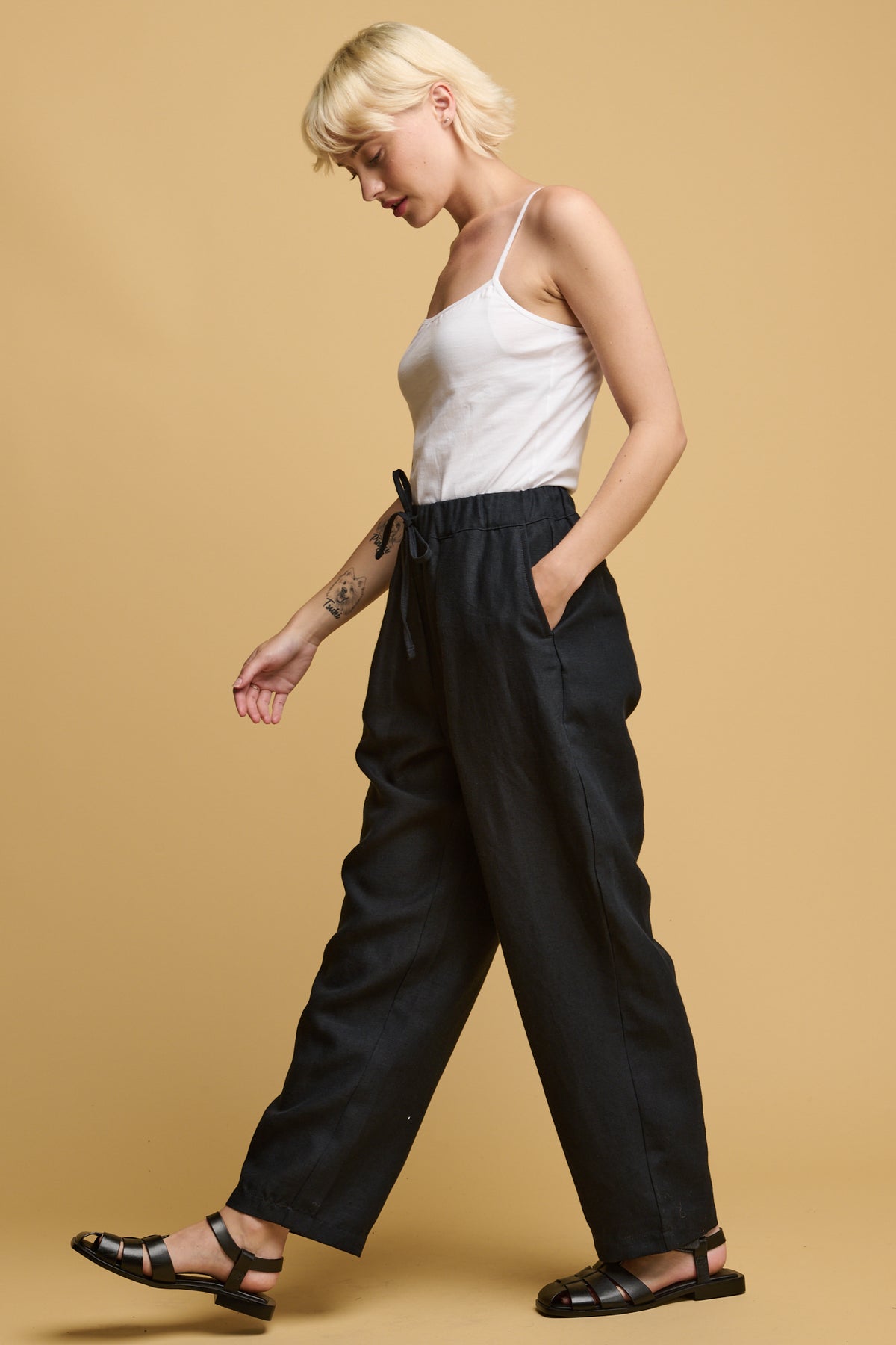 the side of female with short blonde hair wearing white camisole tucked into lorna elasticated waist linen trouser with adjustable drawstring tied into a bow