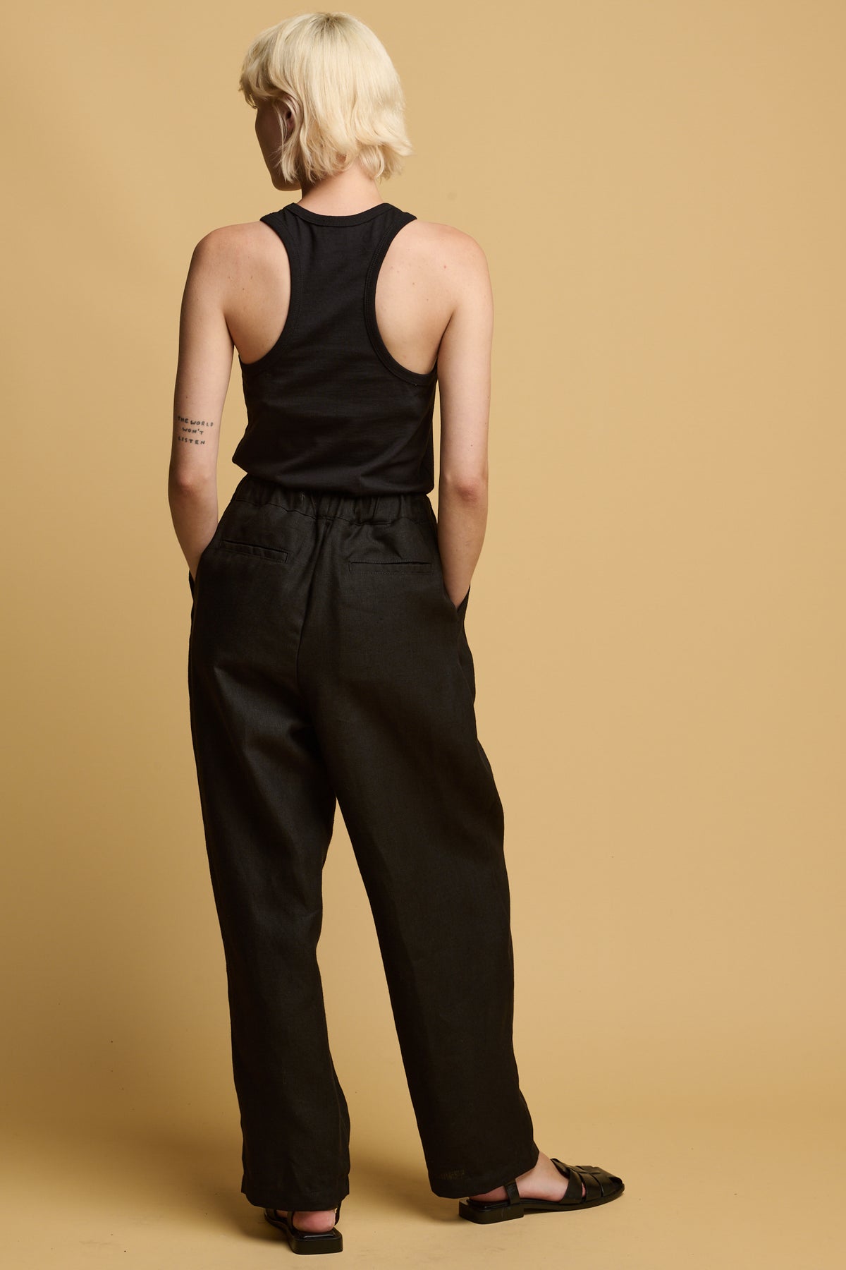The back of female wearing lorna elasticated waist linen trousers in black paired with plastic free racer back vest in black